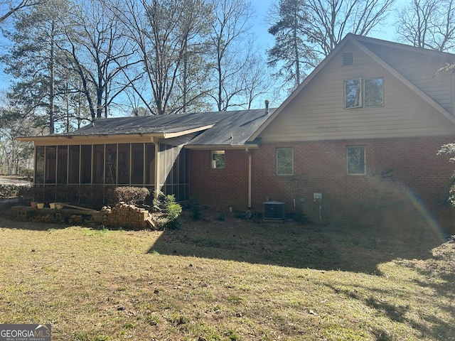 rear view of property featuring a sunroom, central AC unit, a lawn, and brick siding