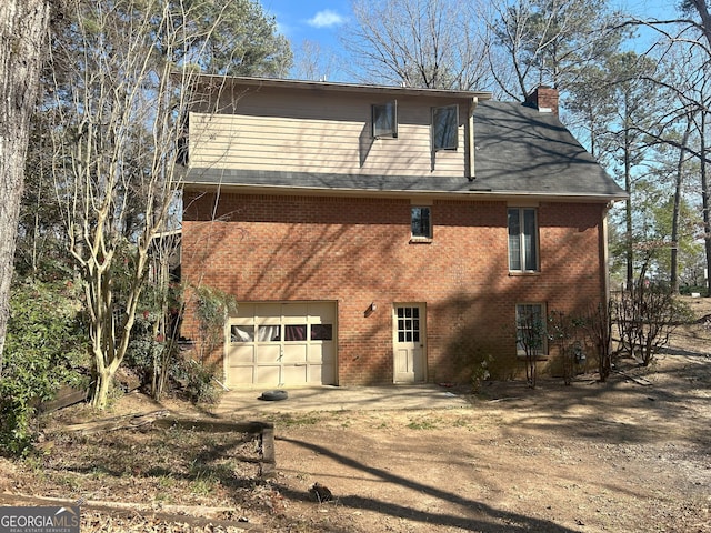 view of front of house with an attached garage, driveway, a chimney, and brick siding