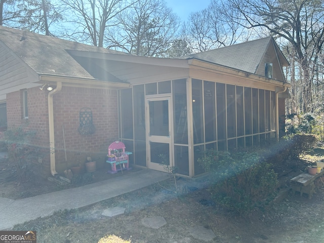 view of side of home with a shingled roof, a sunroom, and brick siding