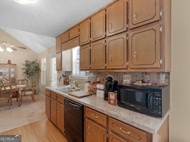 kitchen featuring lofted ceiling, light countertops, decorative backsplash, a sink, and black appliances