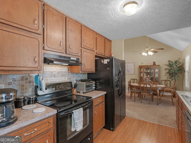 kitchen with vaulted ceiling, black appliances, brown cabinets, and under cabinet range hood