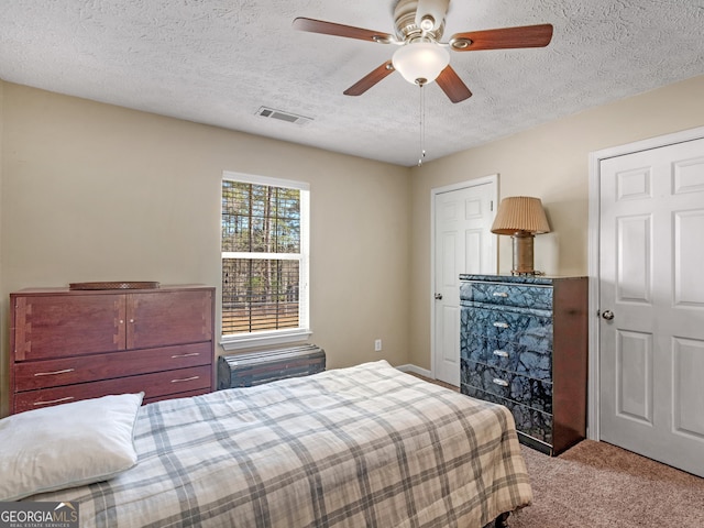 bedroom with a textured ceiling, ceiling fan, carpet flooring, and visible vents