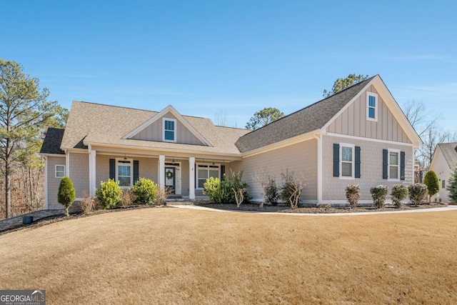 view of front of home with a porch, a front yard, a shingled roof, and board and batten siding