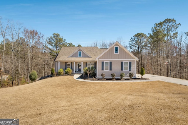 view of front facade with board and batten siding, a front yard, concrete driveway, and covered porch