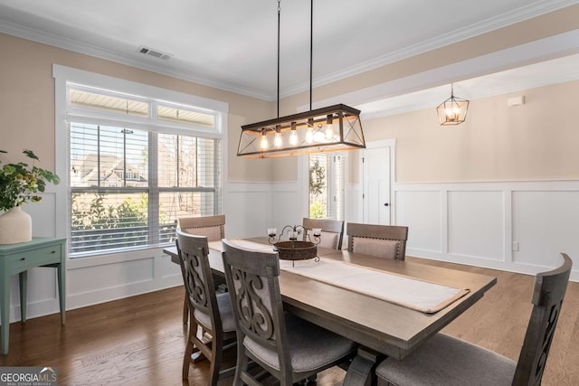 dining room with dark wood-type flooring, wainscoting, visible vents, and crown molding