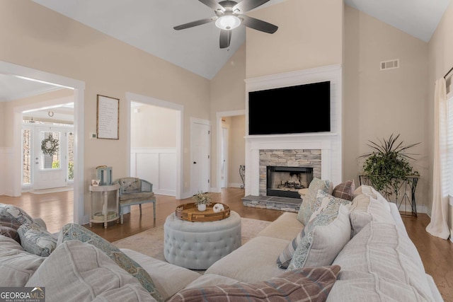 living area with ceiling fan, high vaulted ceiling, a stone fireplace, wood finished floors, and visible vents