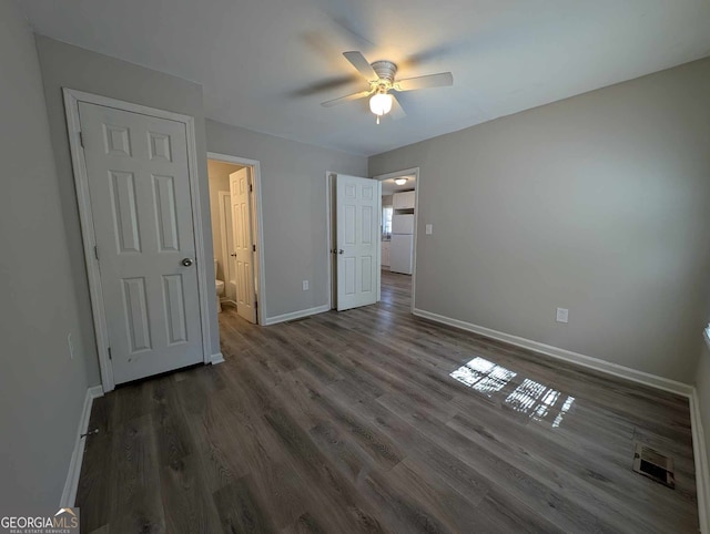 unfurnished bedroom with ensuite bath, baseboards, wood finished floors, and freestanding refrigerator