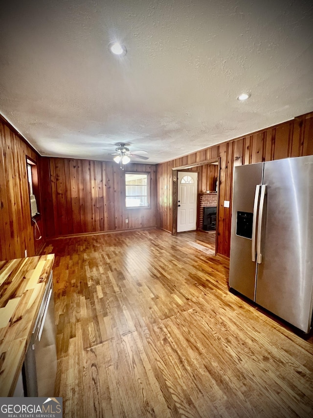 kitchen featuring a textured ceiling, a fireplace, a ceiling fan, light wood-style floors, and stainless steel fridge