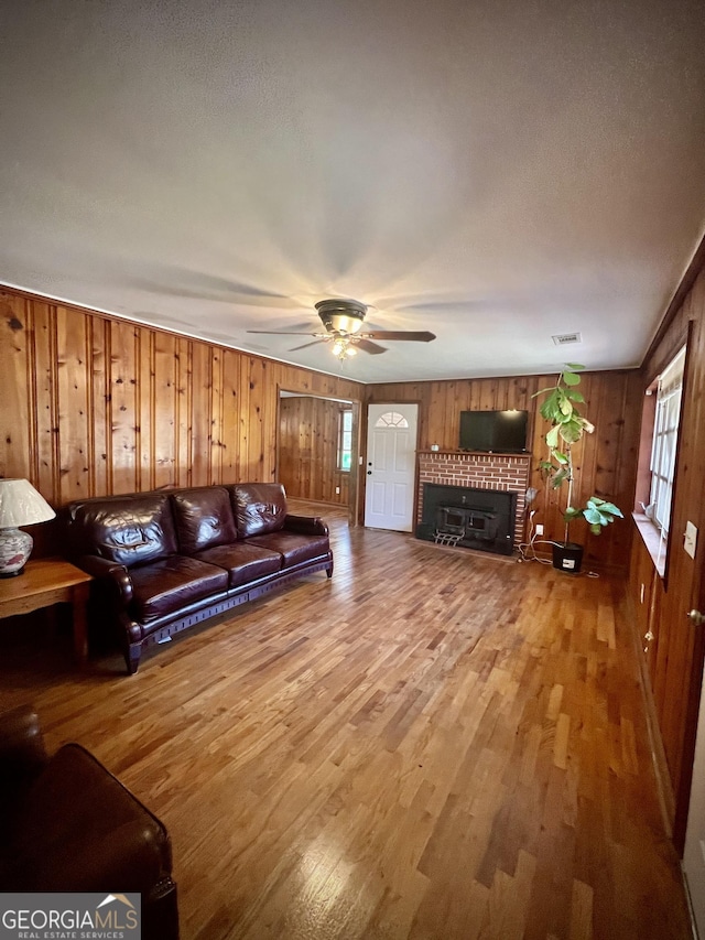 living area with ceiling fan, wood walls, wood finished floors, visible vents, and a brick fireplace