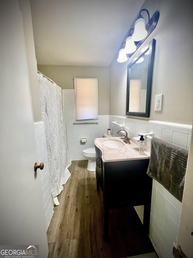 full bathroom featuring toilet, a wainscoted wall, wood finished floors, vanity, and tile walls