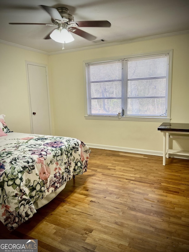 bedroom featuring ornamental molding, multiple windows, baseboards, and wood finished floors