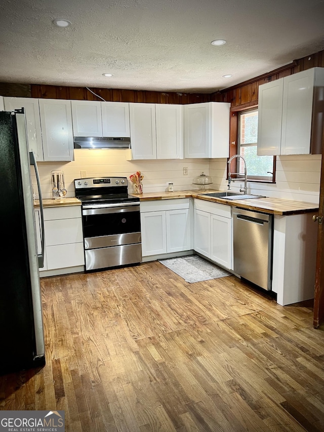 kitchen with stainless steel appliances, butcher block counters, a sink, and under cabinet range hood