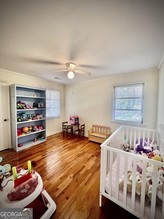 bedroom featuring a crib, visible vents, a ceiling fan, wood finished floors, and crown molding