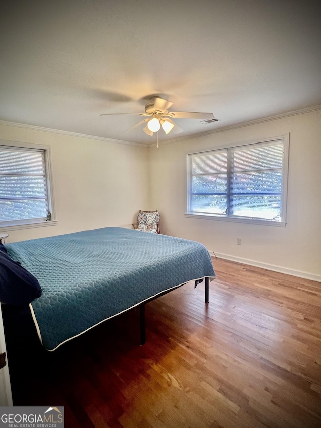 bedroom featuring ornamental molding, multiple windows, visible vents, and wood finished floors