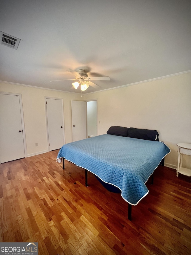 bedroom featuring crown molding, visible vents, a ceiling fan, wood finished floors, and baseboards