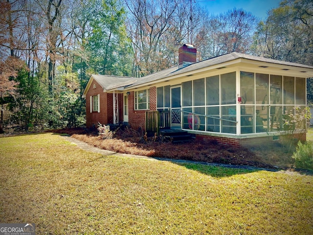 view of side of property with a sunroom, a chimney, a lawn, and brick siding