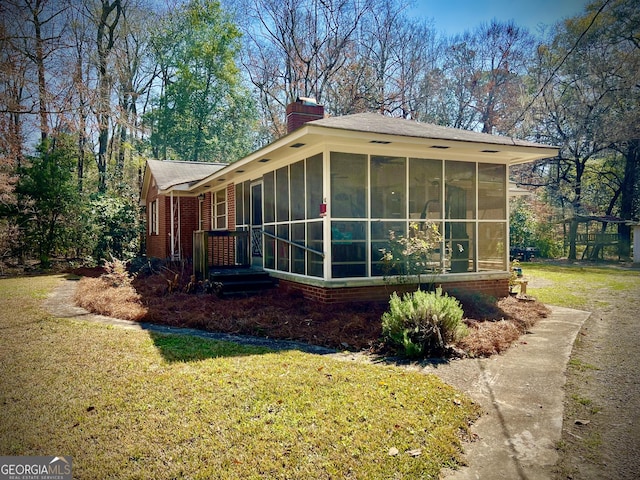 view of side of home featuring a sunroom, a chimney, brick siding, and a yard