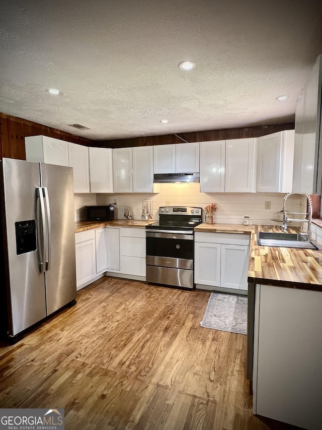 kitchen with light wood-style flooring, under cabinet range hood, a sink, wooden counters, and appliances with stainless steel finishes