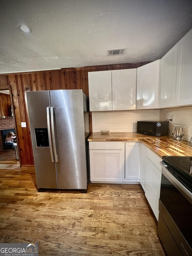 kitchen with light wood finished floors, stainless steel appliances, butcher block counters, white cabinetry, and a textured ceiling