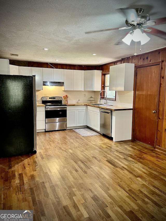 kitchen featuring appliances with stainless steel finishes, white cabinets, a sink, light wood-type flooring, and under cabinet range hood