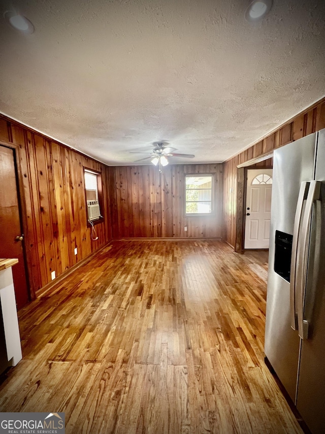 unfurnished living room featuring wood walls, ceiling fan, a textured ceiling, and light wood finished floors