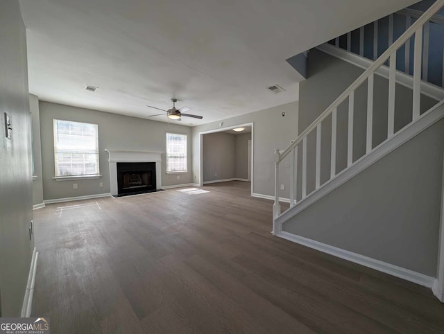 unfurnished living room with a fireplace, wood finished floors, visible vents, a ceiling fan, and stairs