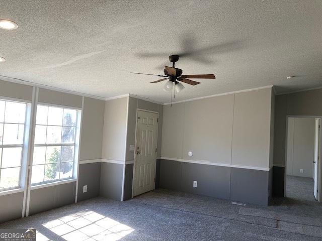 empty room with carpet floors, ornamental molding, a textured ceiling, and ceiling fan