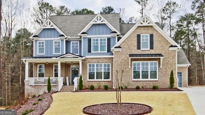 craftsman-style home featuring board and batten siding, a front yard, covered porch, and brick siding