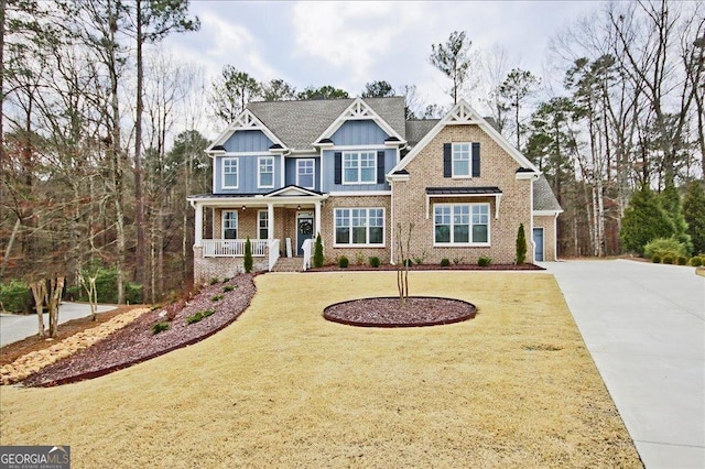 craftsman-style house with a porch, brick siding, concrete driveway, board and batten siding, and a front yard