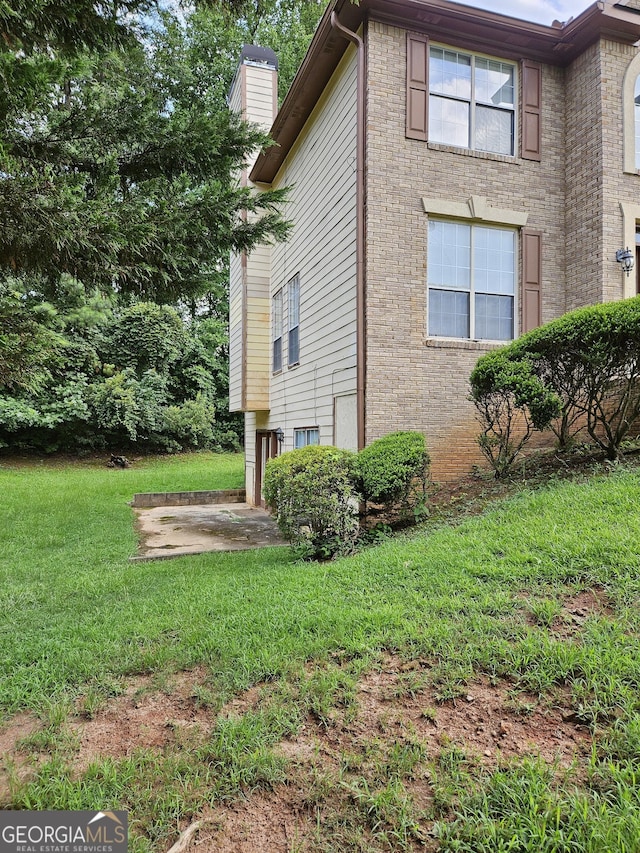 view of side of property featuring a yard, brick siding, a chimney, and a patio area