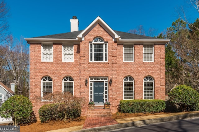 colonial home featuring brick siding and a chimney