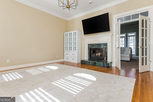 unfurnished living room featuring crown molding, a premium fireplace, wood finished floors, a chandelier, and baseboards