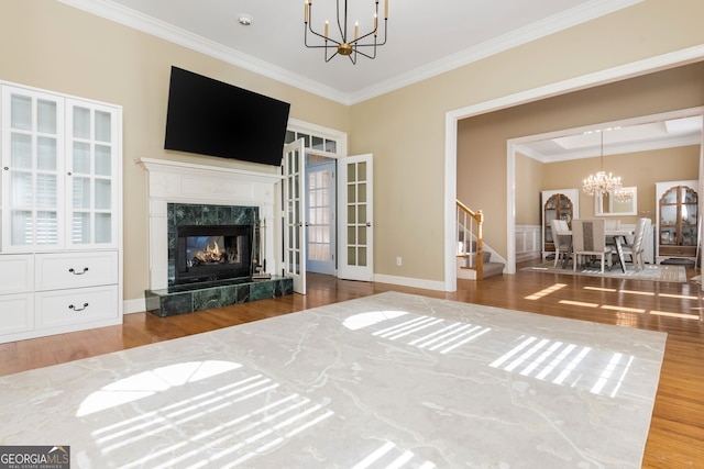 living room with ornamental molding, wood finished floors, an inviting chandelier, stairs, and a high end fireplace