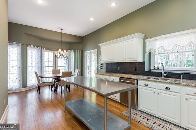 kitchen featuring light wood finished floors, white cabinets, backsplash, stainless steel dishwasher, and a sink