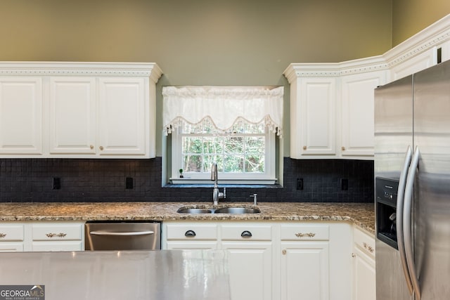 kitchen featuring appliances with stainless steel finishes, white cabinets, a sink, and decorative backsplash