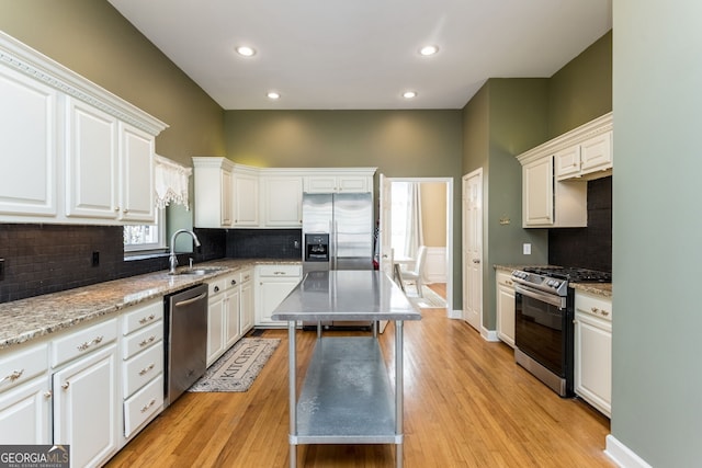 kitchen with white cabinets, a kitchen island, appliances with stainless steel finishes, light wood-style floors, and a sink