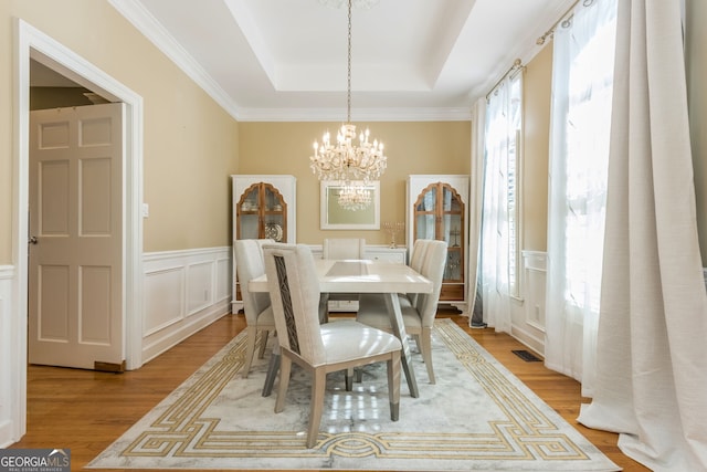 dining room featuring a raised ceiling, visible vents, a decorative wall, a chandelier, and light wood-type flooring