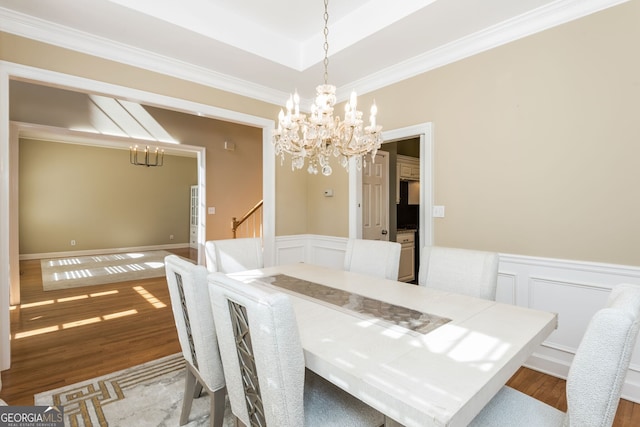 dining space featuring an inviting chandelier, a raised ceiling, wood finished floors, and a wainscoted wall