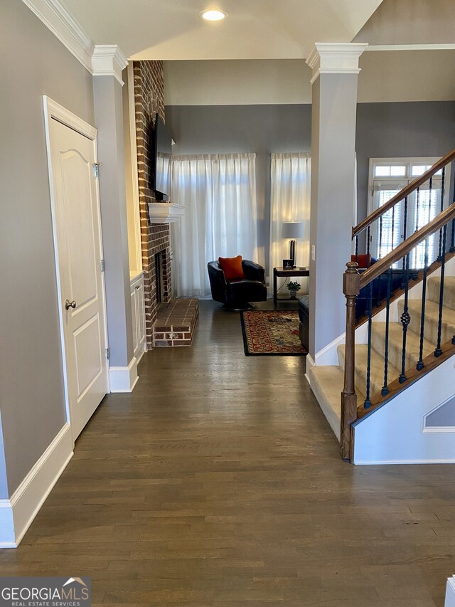 corridor with ornate columns, crown molding, stairs, and wood finished floors