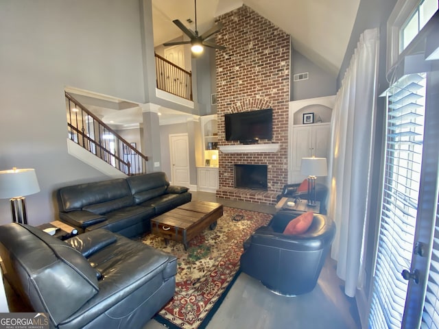 living area with visible vents, a ceiling fan, a brick fireplace, high vaulted ceiling, and stairs