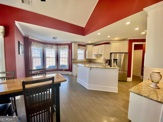 kitchen with dark wood finished floors, stainless steel fridge, crown molding, and light stone countertops