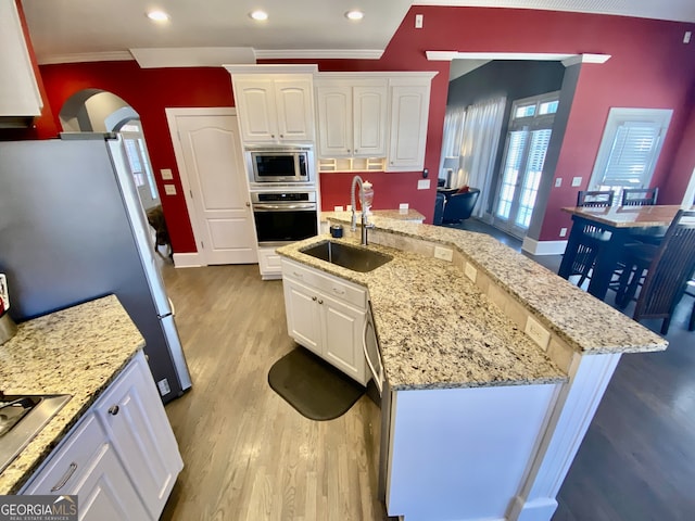 kitchen with arched walkways, stainless steel appliances, light wood-type flooring, white cabinetry, and a sink