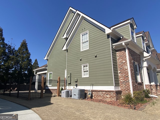 view of side of property featuring brick siding, fence, and central air condition unit