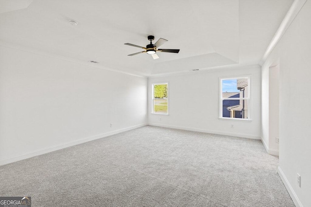 spare room featuring a ceiling fan, a tray ceiling, light carpet, and baseboards