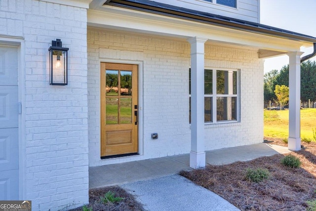 view of exterior entry featuring a garage, covered porch, and brick siding