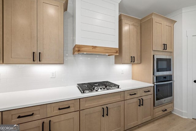 kitchen with stainless steel appliances, light countertops, light wood-type flooring, decorative backsplash, and light brown cabinetry