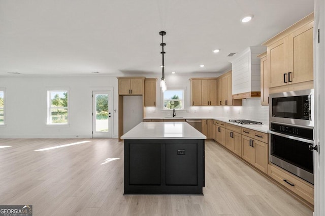 kitchen with light brown cabinets, a sink, a kitchen island, appliances with stainless steel finishes, and wall chimney range hood