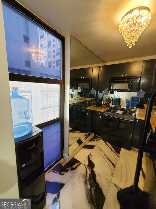 kitchen with marble finish floor, dark cabinetry, black appliances, and an inviting chandelier