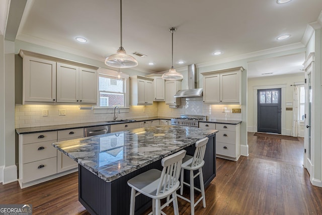 kitchen featuring wall chimney exhaust hood, visible vents, a center island, a sink, and gas range oven