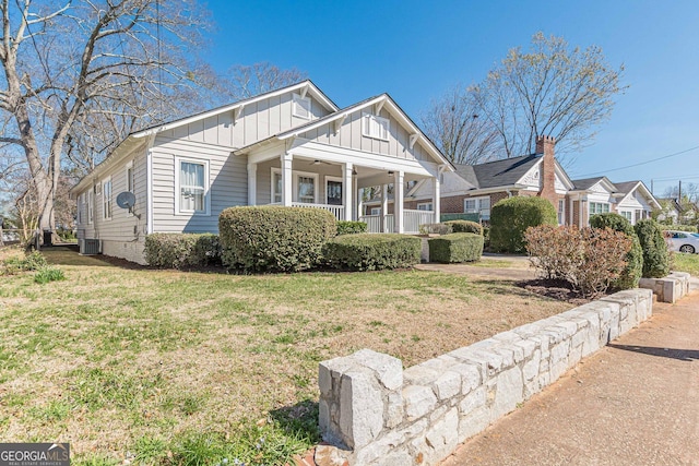 view of front of property with board and batten siding, ceiling fan, a porch, a front yard, and central AC unit
